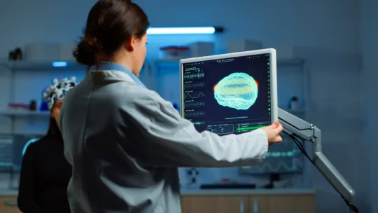 Neuropsicóloga escaneando el cerebro de un paciente Una neuropsicóloga realiza un escáner cerebral a un paciente sentado junto a un monitor, mientras observa la imagen en pantalla