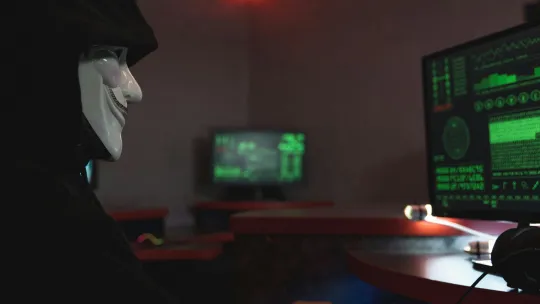 delitos-informaticos-en-colombia hacker-con-mascara-frente-a-computador-ilustrando-los-delitos-informaticos-en-colombia