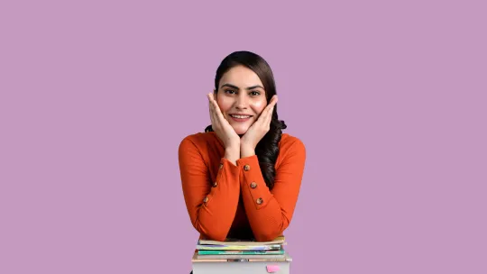 Estudiante preparándose para la especialidad del Máster de Profesorado Estudiante joven sonriente apoyada sobre un bloque de libros, representando la preparación académica para la especialidad en el Máster de Profesorado.