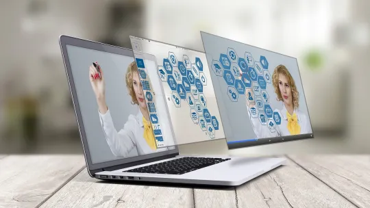 Herramientas digitales para la docencia en el aula Ordenador portátil sobre una mesa de madera mostrando una interfaz virtual con iconos educativos mientras una profesora interactúa con el contenido en pantalla.