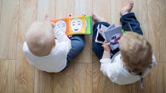 plano-cenital-de-dos-bebes-sentados-en-el-suelo-jugando-con-libros-infantiles-a-los-cuales-les-estan-haciendo-estudios-sobre-neuropsicologia-infantil