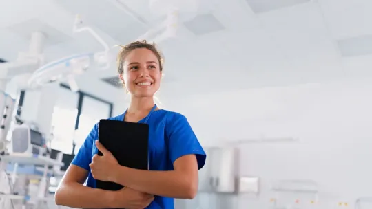 Profesional de enfermería gestionando el triaje hospitalario Una enfermera con uniforme azul sostiene una tableta digital en una unidad de triaje en enfermería hospitalaria.
